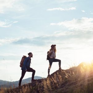Young tourist couple travellers with backpacks hiking in nature at sunset.